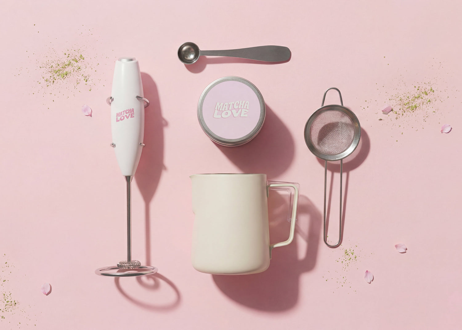 Set of matcha tools including a hand mixer, mug, and strainer on a pink background