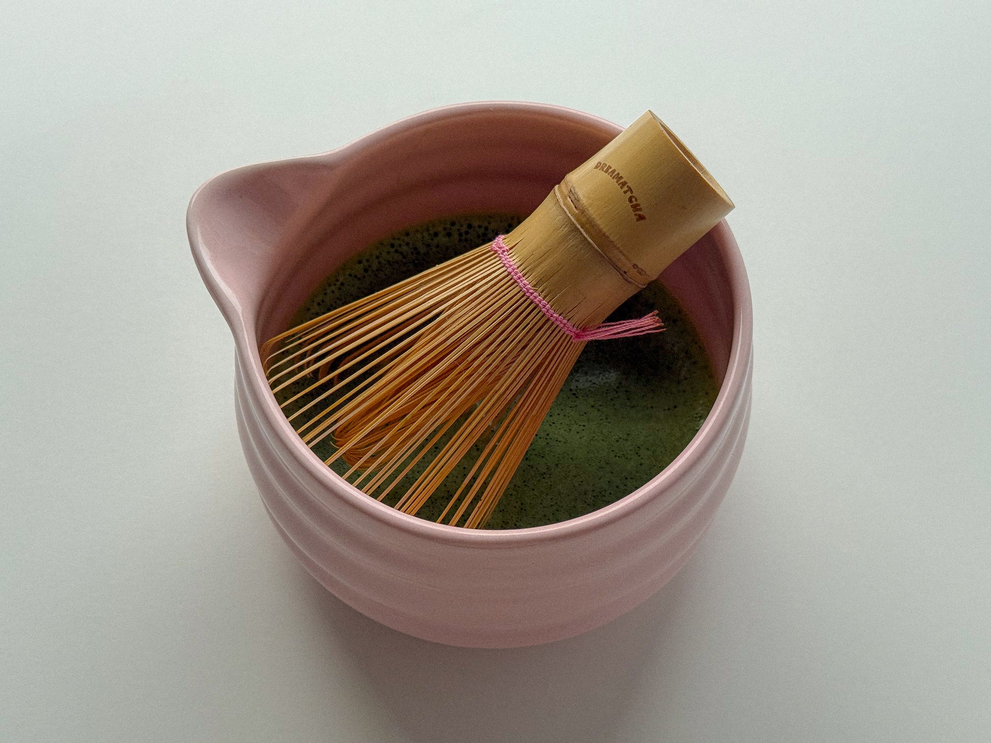 Pink ceramic whisk bowl with a bamboo whisk on a white background