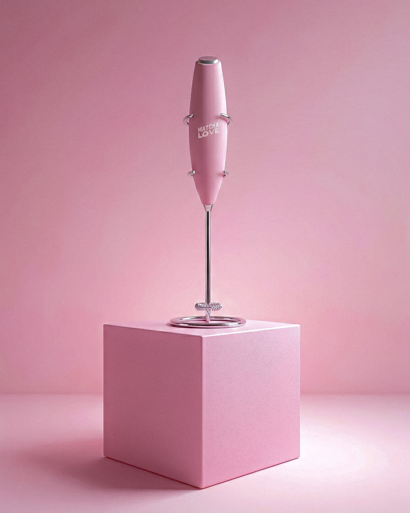 Pink handheld milk frother on a pink cube with a pink background