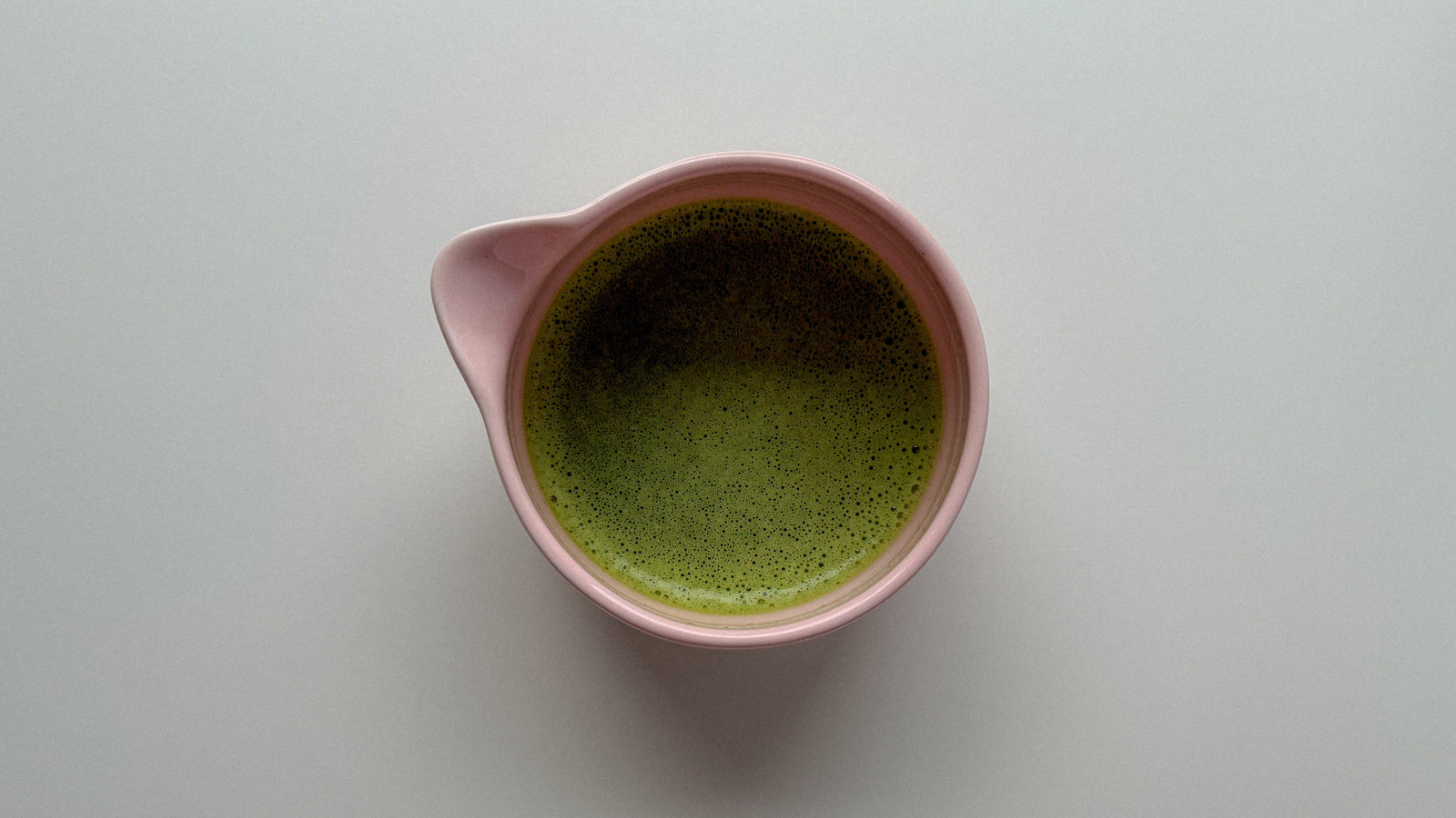 Pink pitcher filled with foamy matcha on a white background