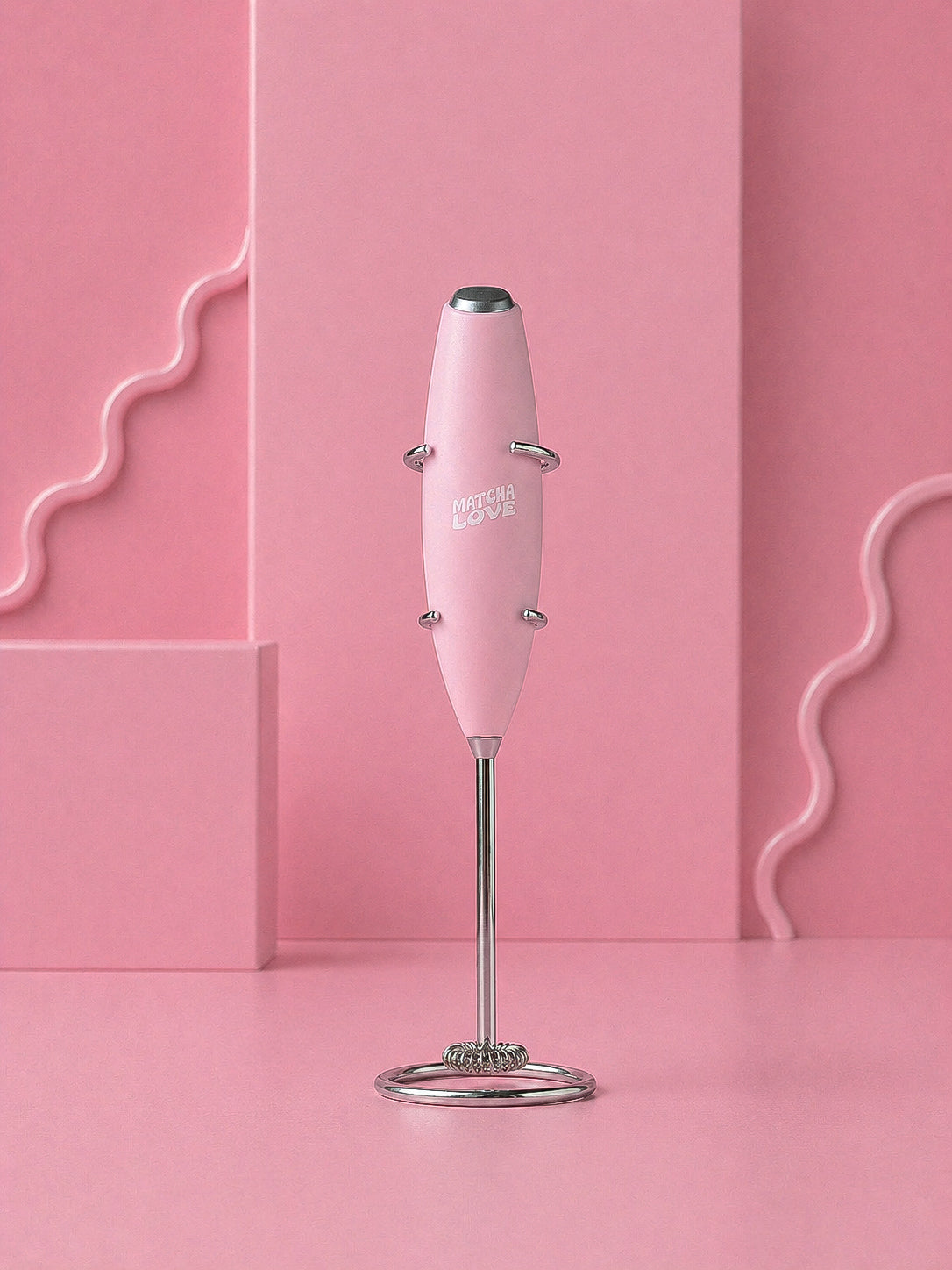 Pink handheld milk frother with metal stand on a pink background