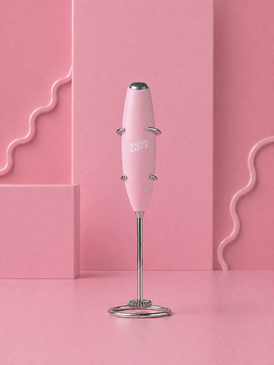 Pink handheld milk frother with metal stand on a pink background